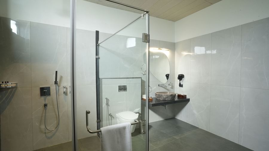 A bathroom of Pool View Room equipped with a glass-enclosed shower, a toilet, and a sink, featuring clean lines and a minimalist design at The Qualia Resort Club & Brewery, Udaipur.