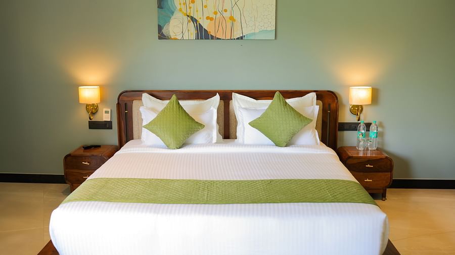 Club Suite with Valley View Sitout featuring a king size bed with white linens and green accents, flanked by bedside tables and lamps at The Qualia Resort Club & Brewery, Udaipur.