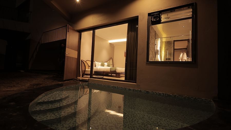 Luxury Villa with Plunge Pool featuring an outdoor pool area at night, with ambient lighting and seating visible through glass windows at The Qualia Resort Club & Brewery, Udaipur.