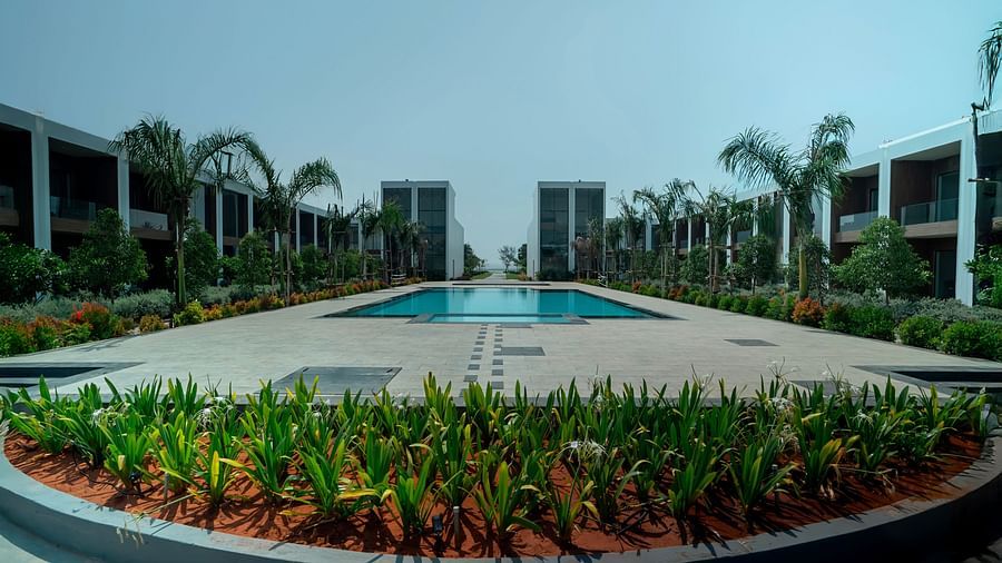 A huge swimming pool in the middle of The Shore Trishvam, Pondicherry with green plants in the foreground.