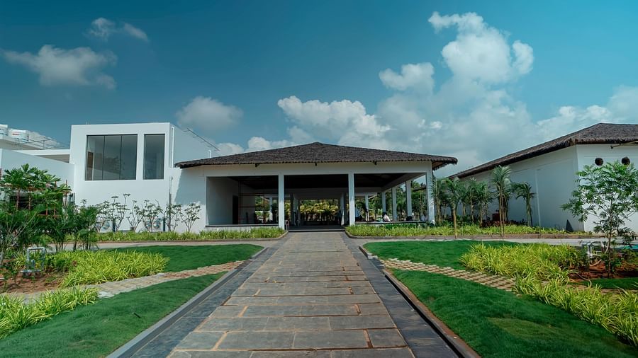 A wide pavement leading to the entrance of The Shore Trishvam, Pondicherry with a sparsely cloudy blue sky in the background.