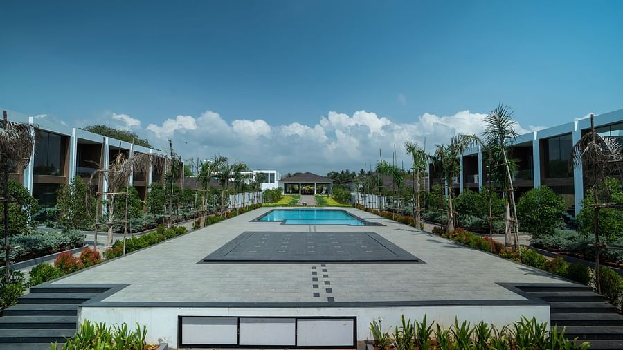 The swimming pool at The SHore Trishvam, Pondicherry surrounded by concrete pathways and trees on a sunny afternoon.