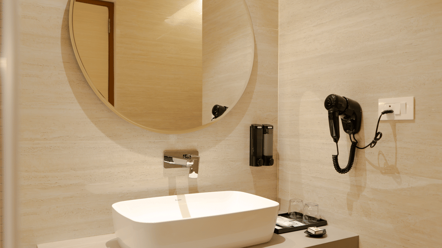 Clean and elegant bathroom of Pearl Villa at The Shore Trishvam, Pondicherry, with vessel sink, round mirror & wall-mounted hairdryer.
