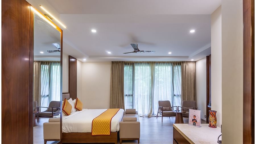 An image of a bed room with king size bed, a dressing tabel with mirror, a table at one corner  and two chairs at another corner - The Silver Sky