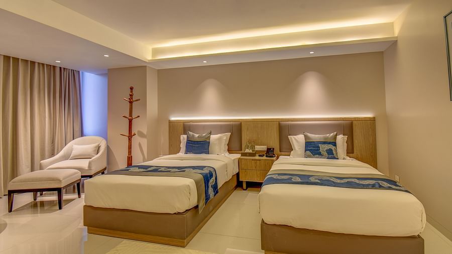 A well-lit Premium Twin room at The SSK Solitaire Boutique Hotel & Spa, Gangapur Road - Nashik featuring a twin  bed, two armchairs, a small table, and a work desk with a chair.