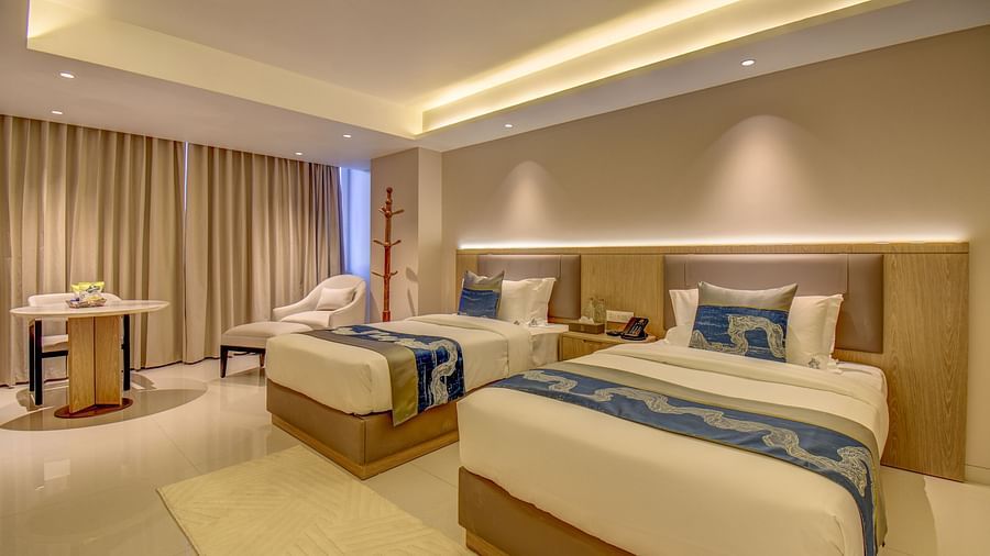 Side view of a well-lit Premium Twin room at The SSK Solitaire Boutique Hotel & Spa, Gangapur Road - Nashik featuring a twin  bed, two armchairs, a small table, and a work desk with a chair.