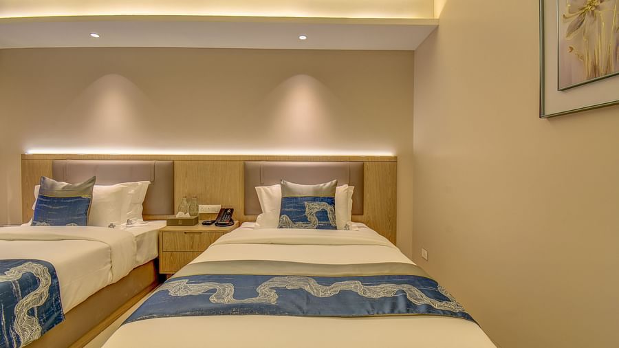 Close up of a well-lit Premium Twin room at The SSK Solitaire Boutique Hotel & Spa, Gangapur Road - Nashik featuring a twin  bed, two armchairs, a small table, and a work desk with a chair.