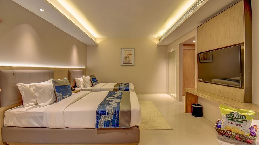Side view of a well-lit Premium Twin room at The SSK Solitaire Boutique Hotel & Spa, Gangapur Road - Nashik featuring a twin  bed, two armchairs, a small table, and a work desk with a chair.