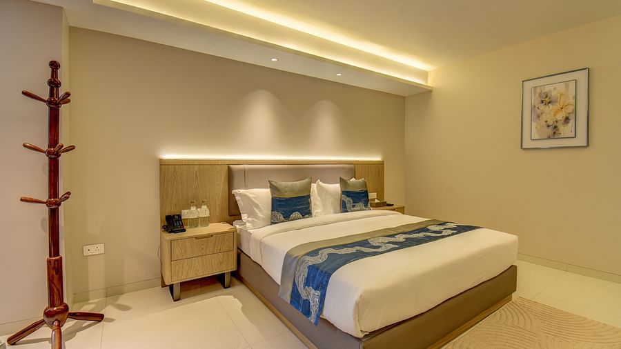 Side shot of a  well-lit Deluxe King room at The SSK Solitaire Boutique Hotel & Spa, Gangapur Road - Nashik featuring a king size  bed, two armchairs, a small table, and a work desk with a chair.