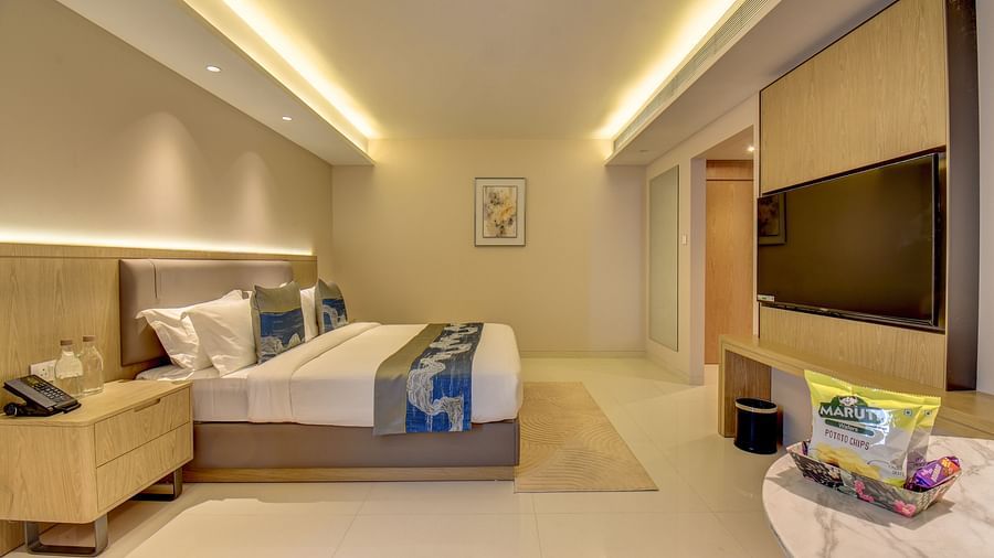 A well-lit Deluxe King room at The SSK Solitaire Boutique Hotel & Spa, Gangapur Road - Nashik featuring a king size  bed, two armchairs, a small table, and a work desk with a chair.