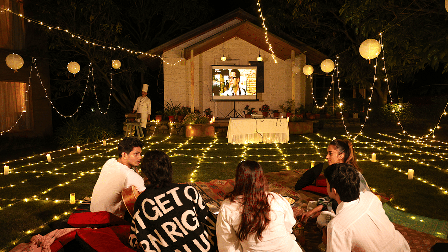 People enjoying an open movie night setup with lights and a projector set up at The Sylvan Retreat, Dehradun. 