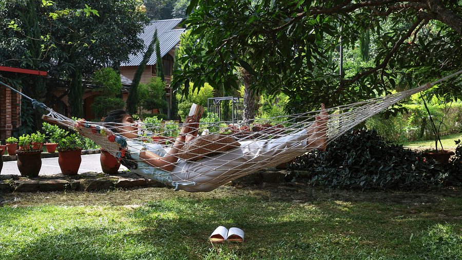 A woman laying on a hammock reading a book at A man flying a kite at The Sylvan Retreat, Dehradun.