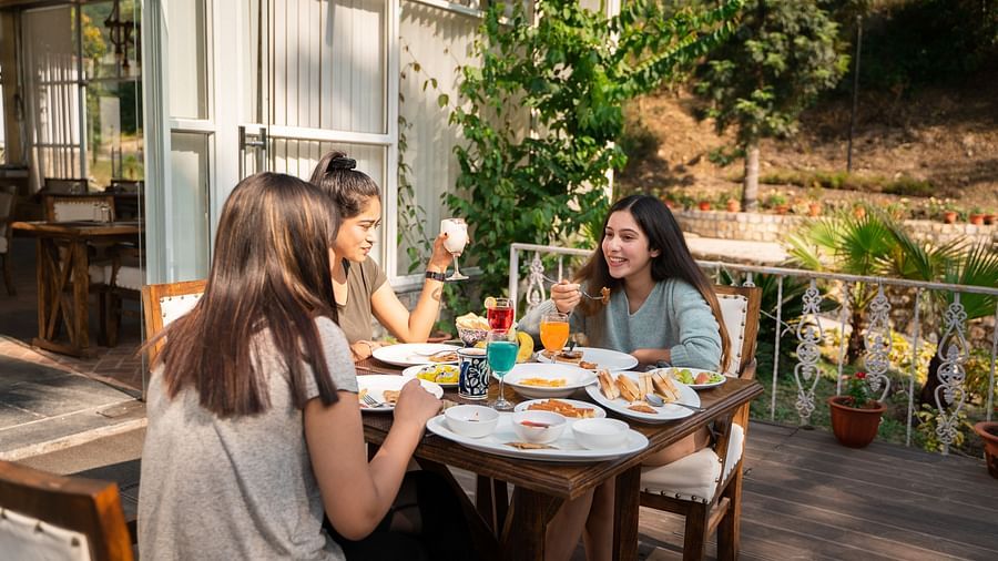 Three women enjoying food in an open setting of Bread and Brook at the Sylvan Retreat, Dehradun.