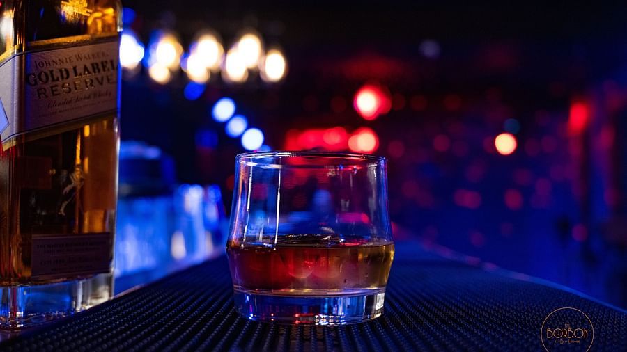 a close up image of a glass holding whisky in a dimly lit bar counter at the bourbon club and lounge - The Tattva Boutique Resort