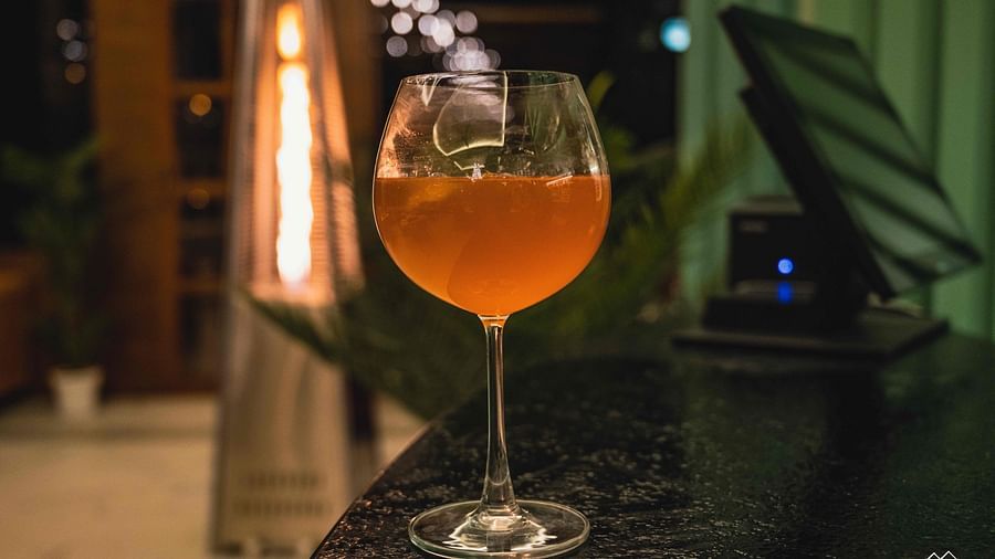image of an orange coloured beverage served in a wine glass kept on a black platform at the alpenrose restaurant - the tattva boutique resort