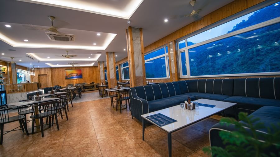 A restaurant at The Tattva Devaprayag with tables and blue chairs and a view of the mountains.