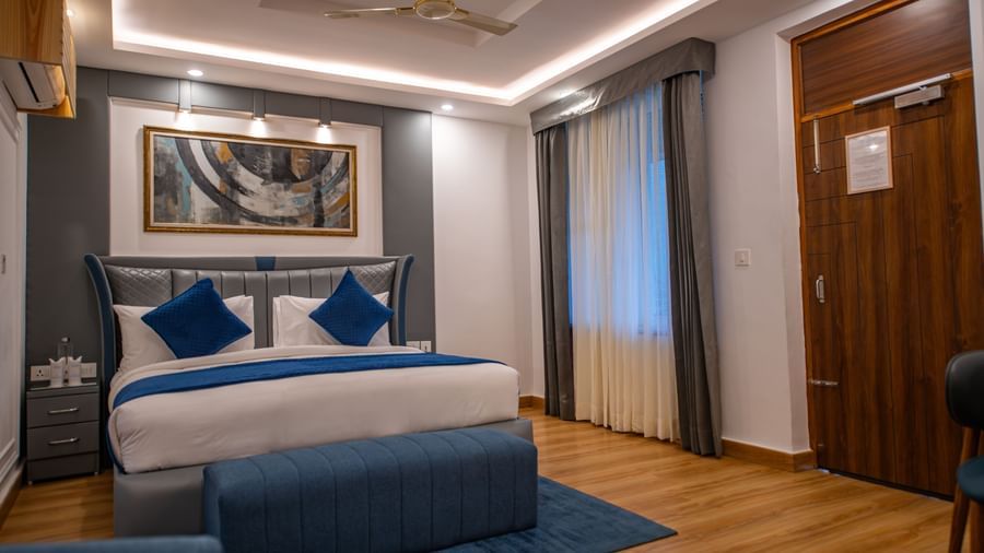 A Superior Room at The Tattva Devaprayag with a bed featuring blue blankets and two pillows, a sofa, and a framed painting on the wall.