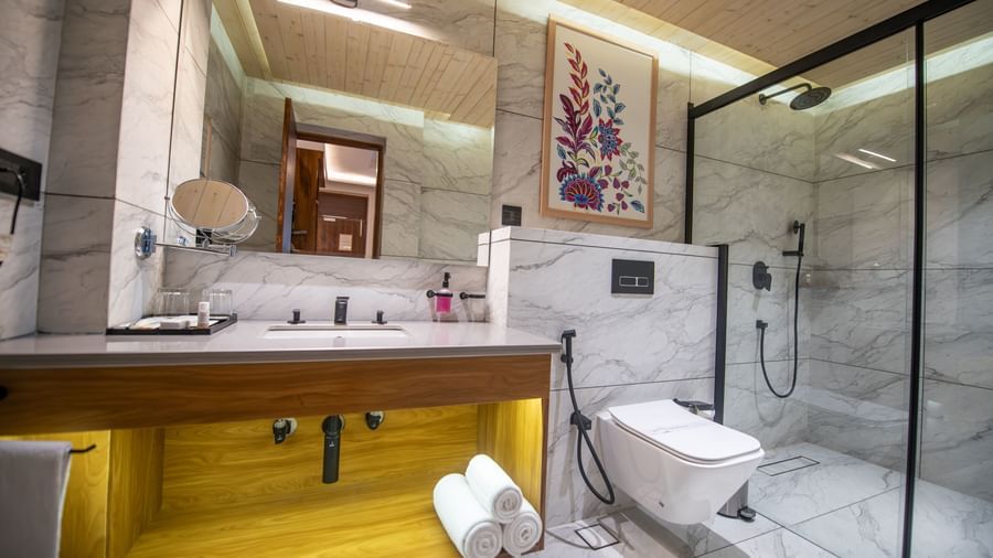 A bathroom in The Tattva Devaprayag with a toilet, a wooden sink, and a shower with a glass door.