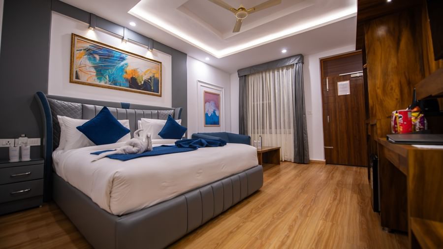 A well-lit Eecutive Room at The Tattva Devaprayag with a bed featuring blue blankets and two pillows, and a framed painting on the wall.V EX0522