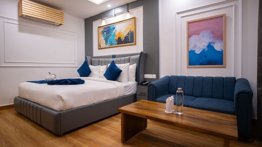  An Executive Room at The Tattva Devaprayag with a bed featuring a blue sofa and two framed paintings on the wall.
