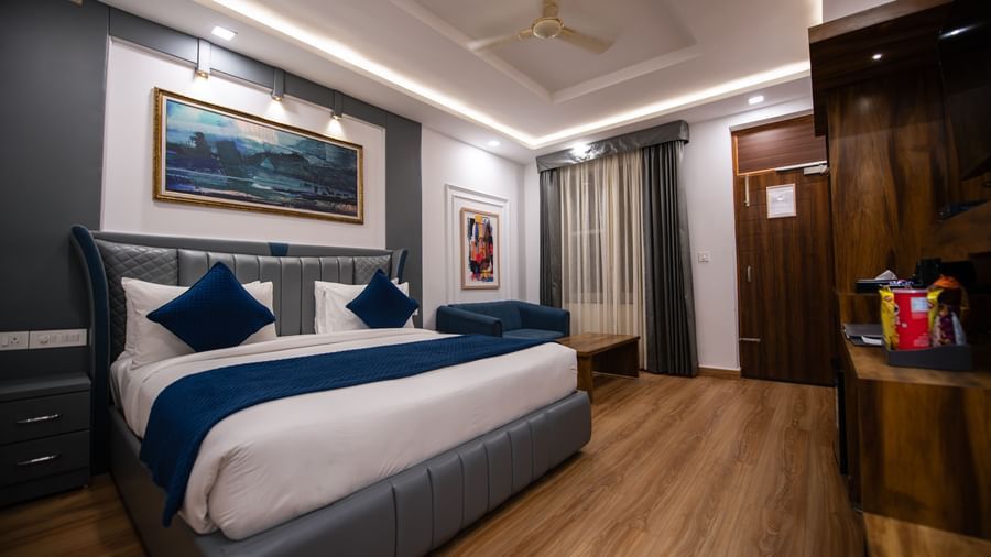 An Executive Room at The Tattva Devaprayag with a bed featuring blue blankets and two pillows, a wooden cabinet, and a framed painting on the wall.