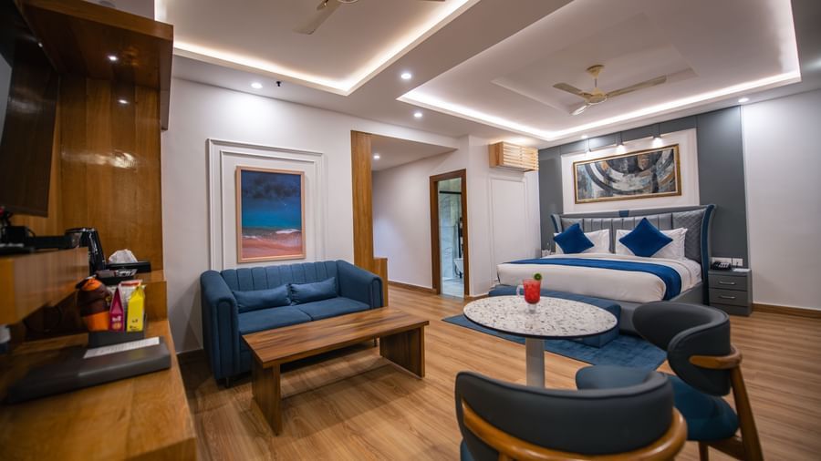 A spacious superior room at The Tattva Devaprayag with a bed featuring blue blankets, a sofa, and a round table.
