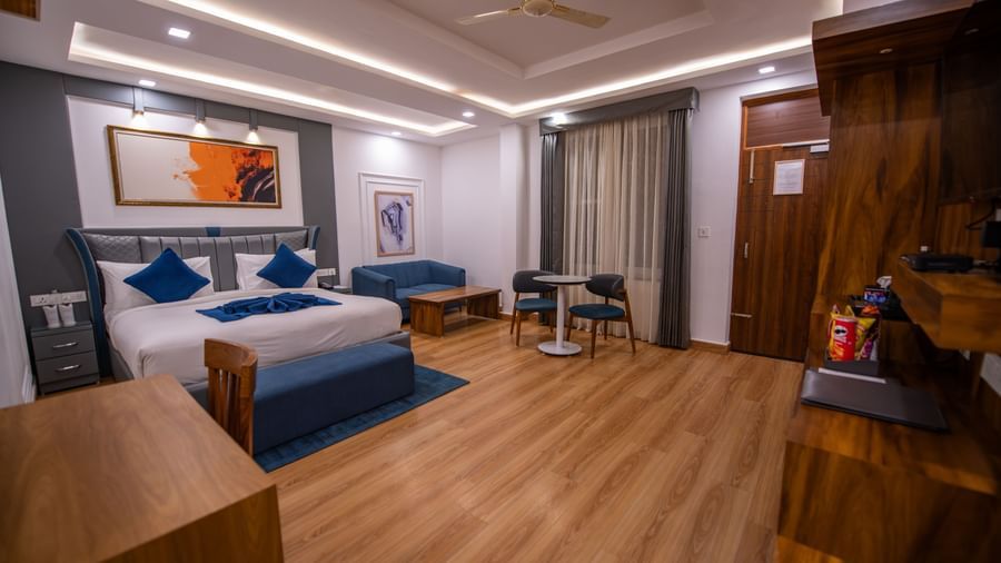 A superior room at The Tattva Devaprayag with a bed dressed in blue blankets and two pillows, a sofa, and framed paintings on the wall.