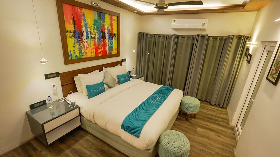 Bedroom of Pent House at The Tattva, Joshimath with a large bed, teal accents, abstract wall art, wooden flooring, grey curtains, and ambient ceiling lighting.