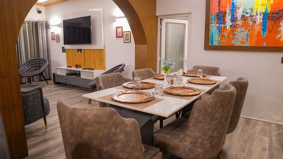 Modern dining and living room of the Pent House at The Tattva, Joshimath with neutral décor, abstract wall art, stylish furniture, and a wooden arch separating both spaces