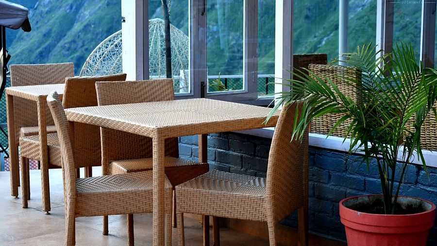 image of an outdoor dining area with chairs arranged besides the huge windows with mountain views in the background from the tattva, joshimath