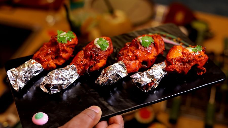 Tandoori chicken drumsticks lined up on a rectangular slate, garnished with lime and cilantro - Themis Barbecue House, Ambience Mall, Gurugram