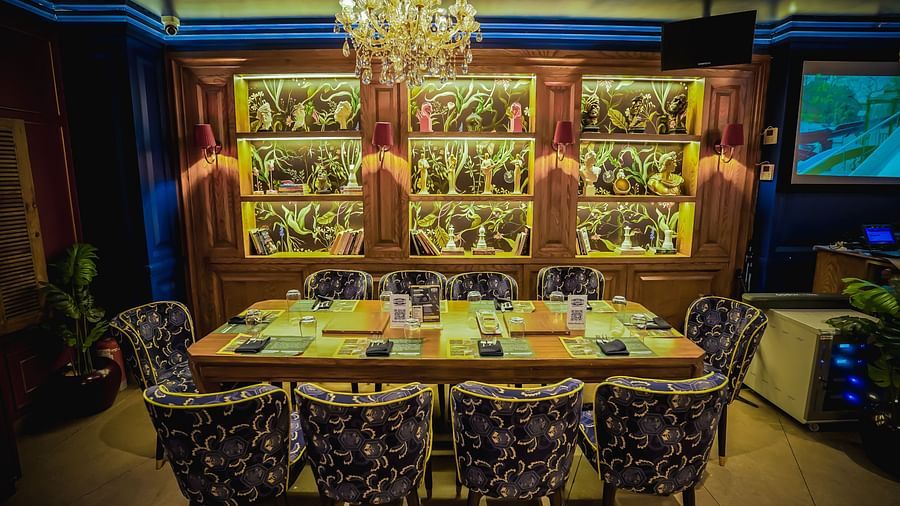 A dining table with 10 chairs around and a chandelier on the top at the restaurant Themis Barbecue House NSP Pitampura
