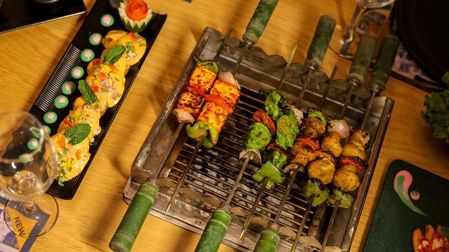 An image of a barbecue set up with meat stuck on skewers along with leafy vegetables at Themis Barbecue House, NSP Pitampura