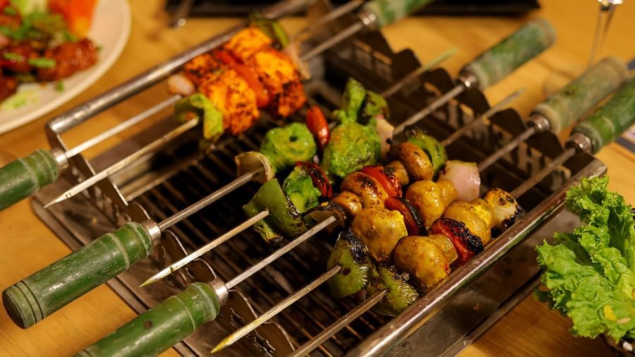 An image of a barbecue set up with meat stuck on skewers along with leafy vegetables - Themis Barbecue House, NSP Pitampura