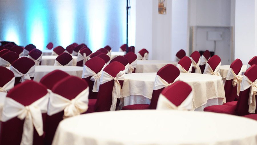 Banquet hall arrangement featuring round tables with white cloths and covered chairs at Tiara by MPS.