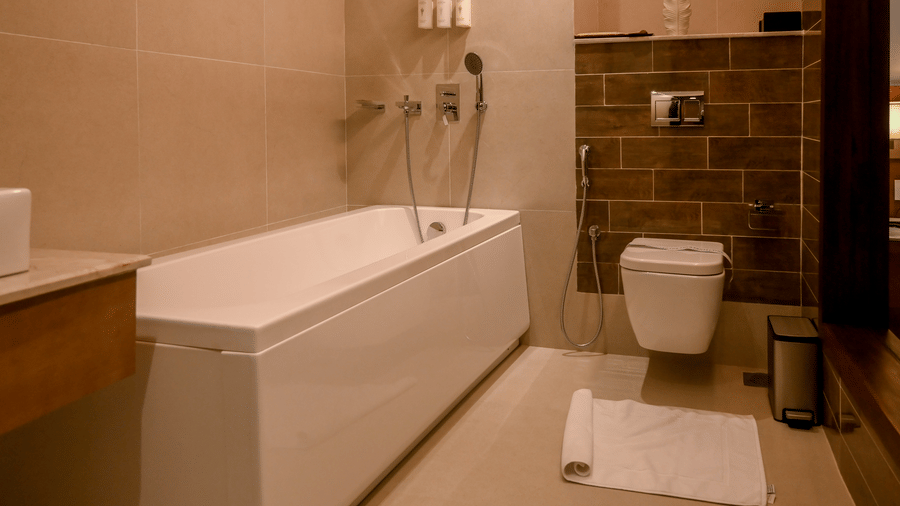 A bathroom view highlighting a bathtub on the left and a toilet set against a brick-patterned wall at Tiara by MPS.