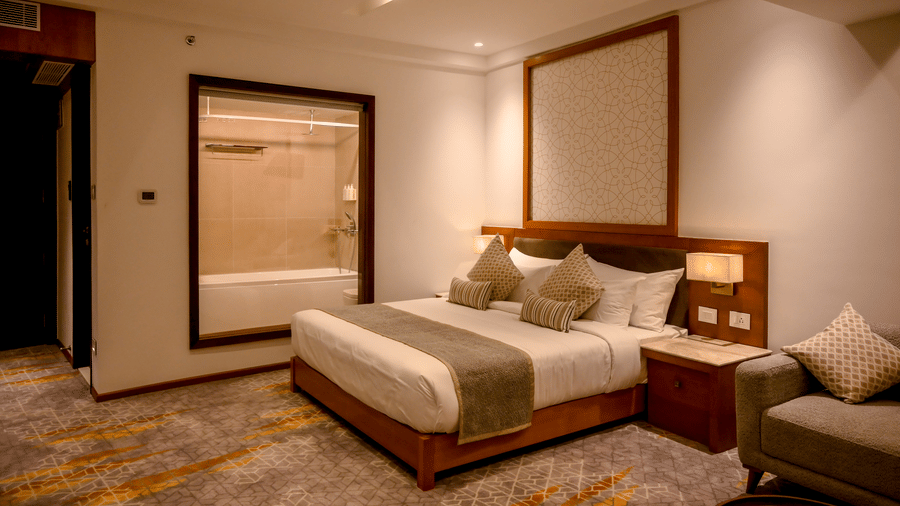 A carpeted bedroom featuring a king size bed and a large glass window viewing into an en suite bathroom at Tiara by MPS.