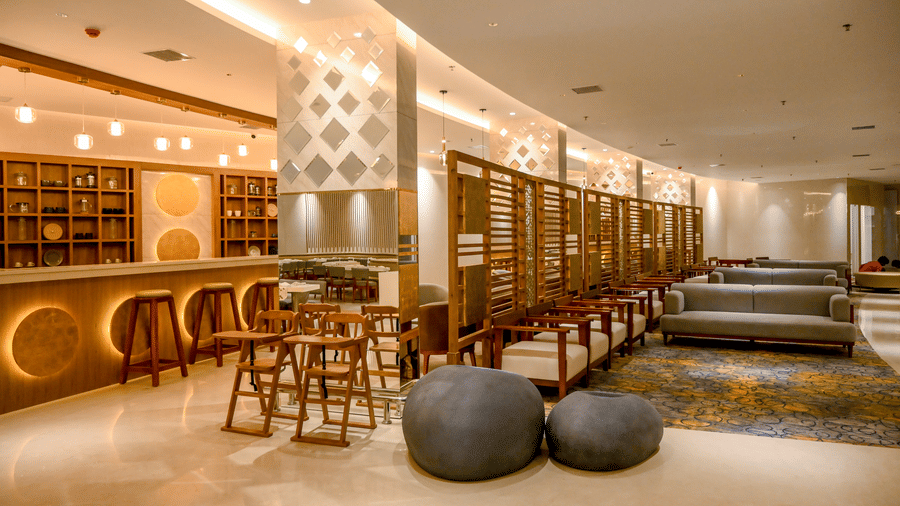 A lounge area featuring contemporary sofas, bean bags, low tables, a bar counter with stools, and patterned pillars at Tiara by MPS.