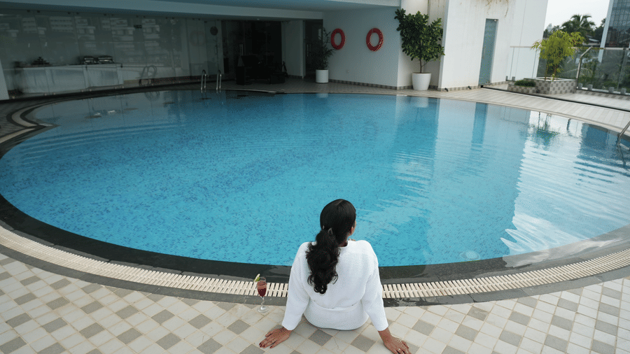 A person sits on the tiled edge looking out over a curved swimming pool at Tiara by MPS.