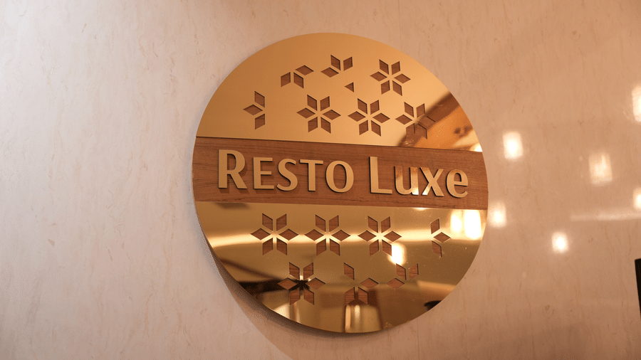 A circular gold reflective sign displays the text RESTO Luxe below 6 star patterns on a light beige wall at Tiara by MPS.