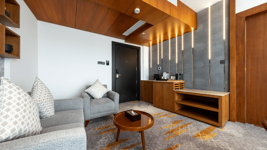A contemporary suite living space with armchair seating, low coffee table, a console unit, and an illuminated feature wall panel at Tiara by MPS.