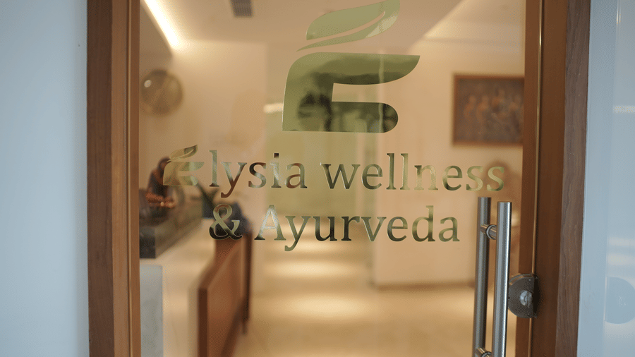 Glass entrance door displaying text for Elysia wellness and Ayurveda at Tiara by MPS leading into a lit hallway.