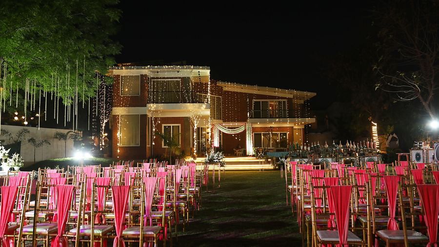 Outdoor event setup at Tisya Farms, Gurgaon with rows of red chairs facing the lit-up main building at night.