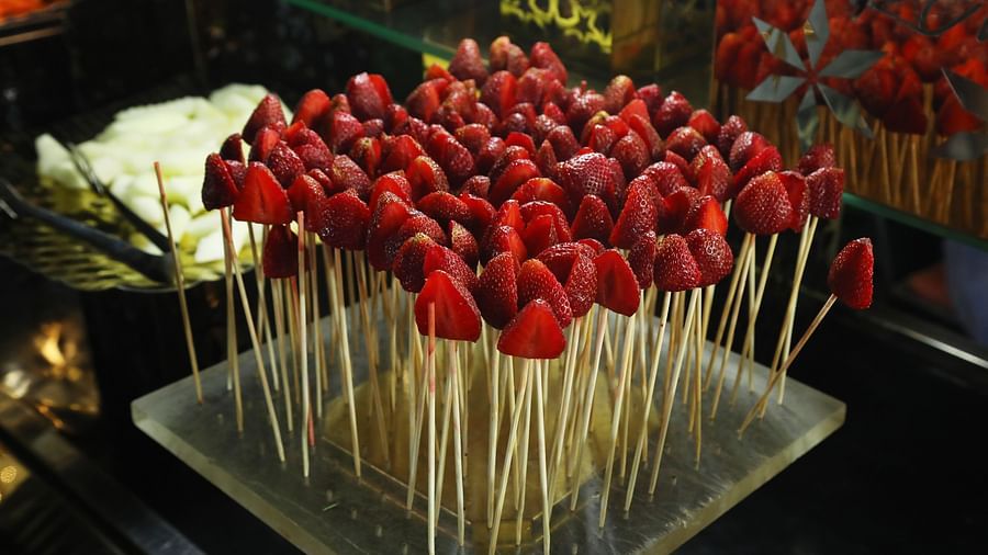 Food display at Tisya Farms, Gurgaon showing skewers of strawberries and grapes on a black tray.