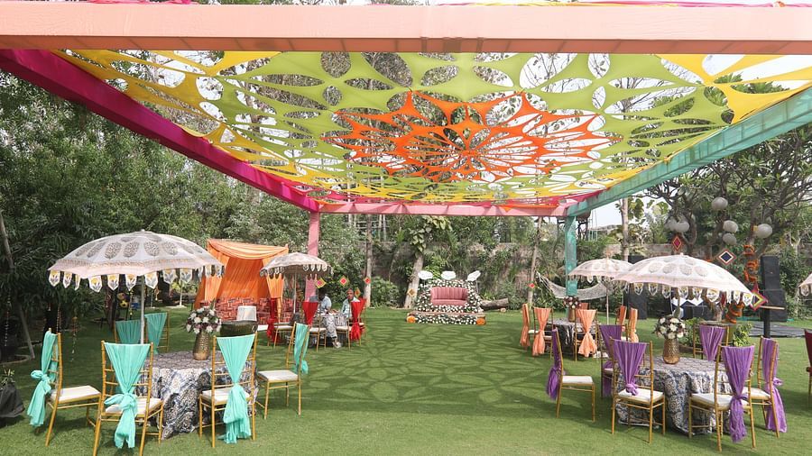 Outdoor seating area at Tisya Farms, Gurgaon with colourful drapes, parasols, and chairs set on a lawn.