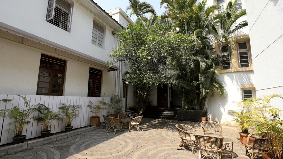 A circular stone courtyard at Trance Sunderban Resort featuring woven chairs, small tables, and potted palms outside the buildings.