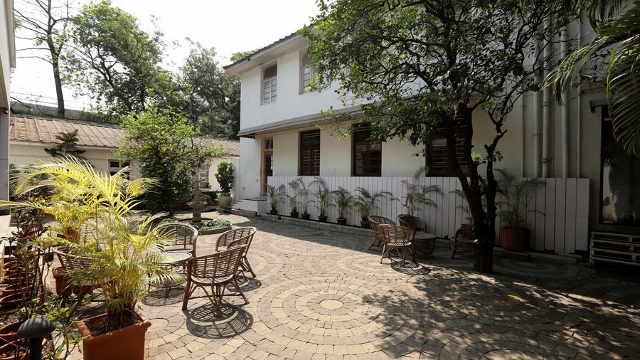 A circular stone courtyard at Trance Sunderban Resort featuring woven chairs, small tables, and potted palms outside the buildings.