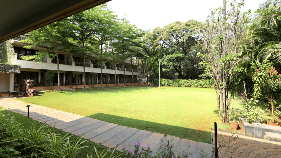 A wide view of a perfectly kept green lawn bordered by a stone path and the resort's guest room wings | Trance Sunderban Resort