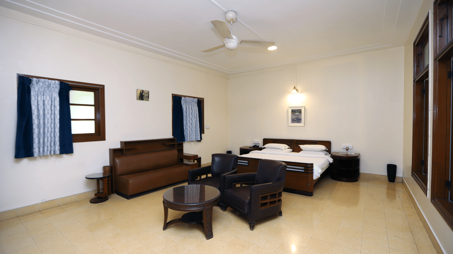 A wide view of the Osho Suite showing a double bed, a wooden sofa set with a coffee table, and cream-coloured walls | Trance Sunderban Resort
