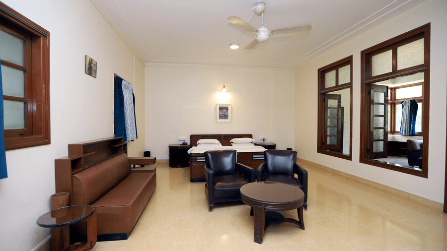 A perspective highlighting the dark wood armchairs and matching sofa, situated across from large wooden-framed windows | Trance Sunderban Resort